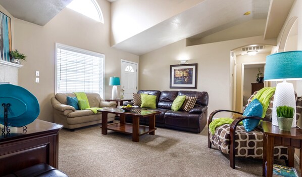 A living room with a beige sofa, a dark leather couch, and a patterned armchair. There is a coffee table in the center, a lamp on a side table, and a framed picture on the wall. - READY IN MERIDIAN.. RELO SPECIALISTS, GOLF COURSE COMMUNITY (Meridian)