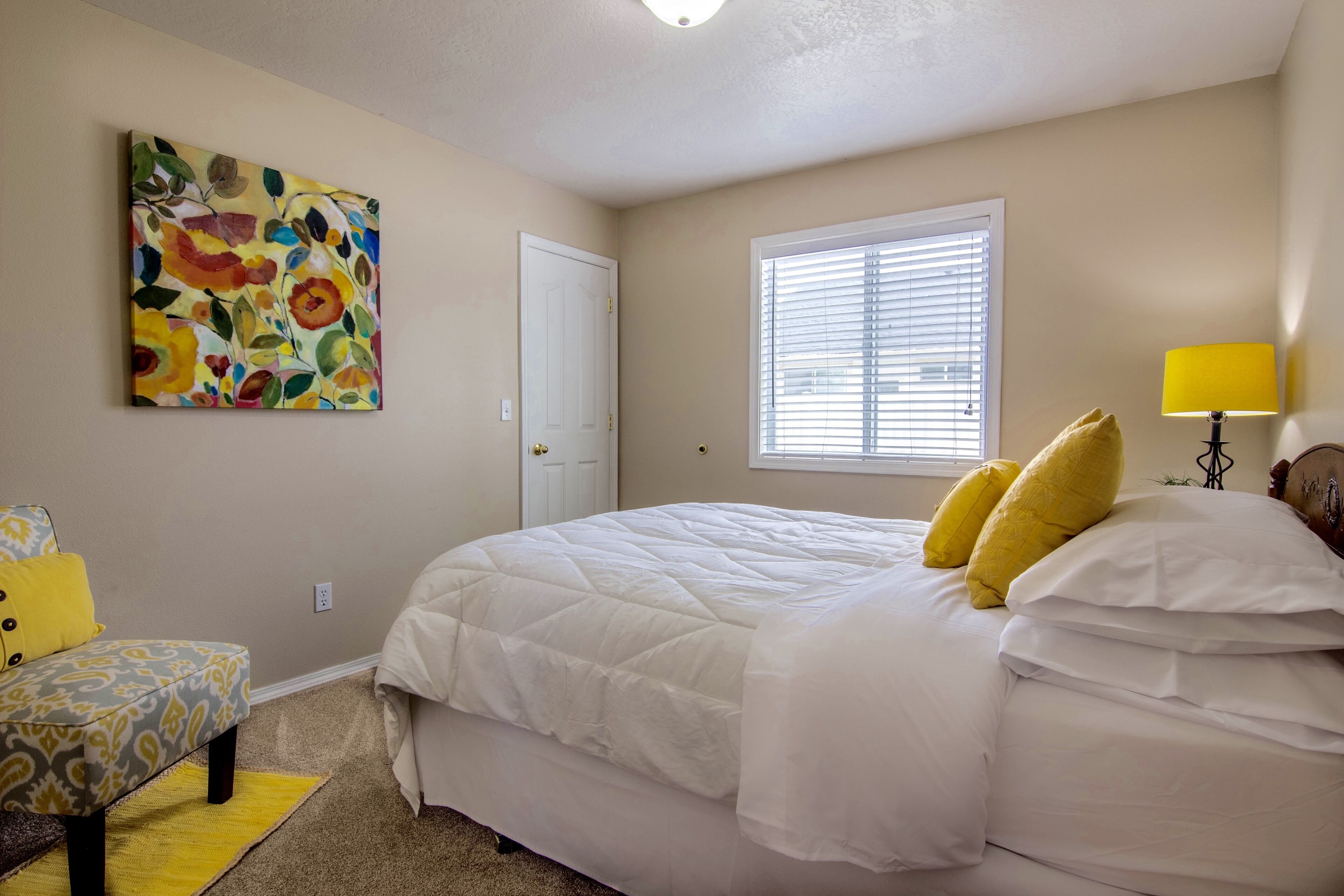 A bedroom with a bed, a chair, a painting, a window, and a lamp.