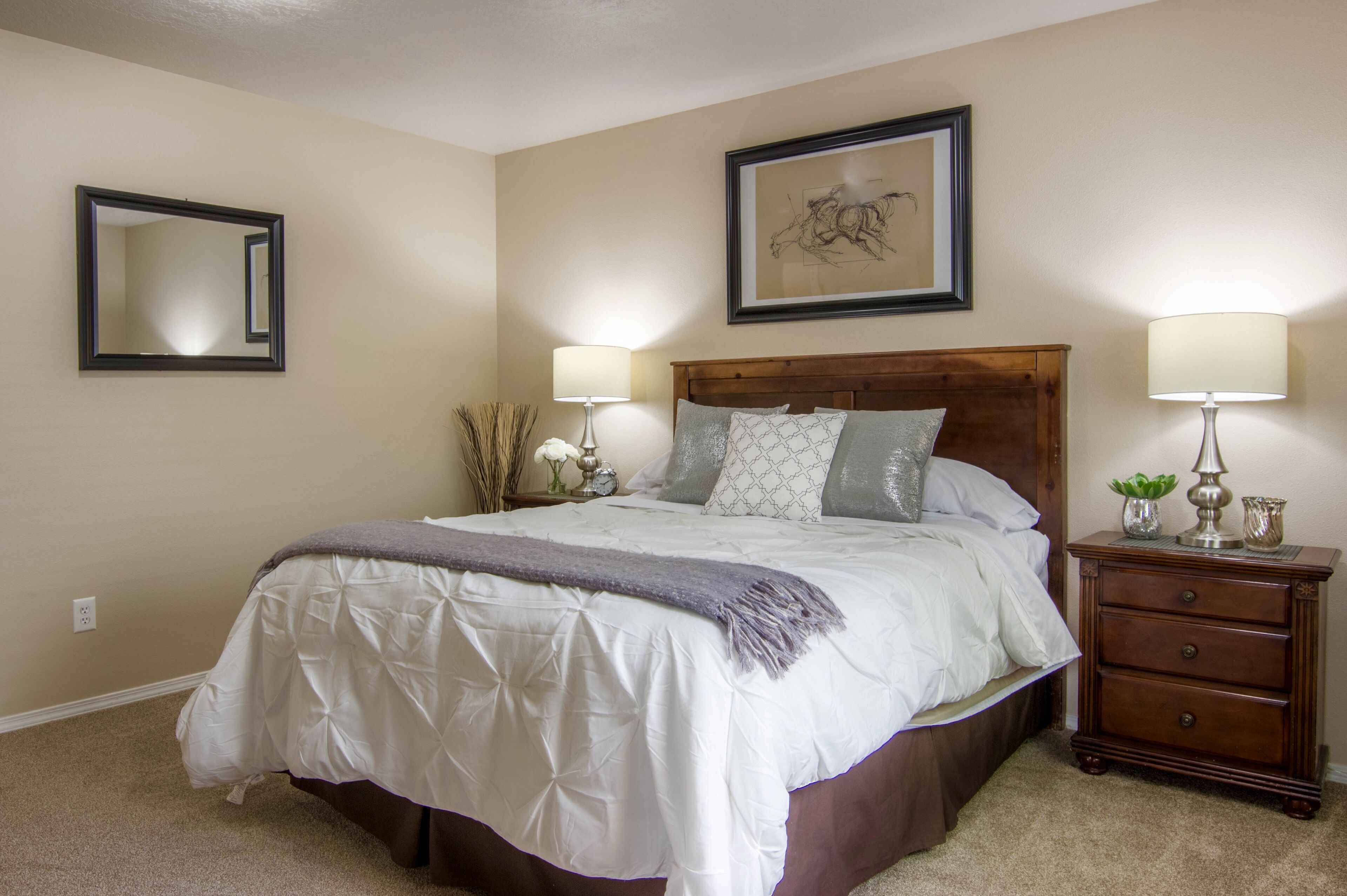 A bedroom with a bed, bedside tables, a mirror, and a framed picture on the wall.