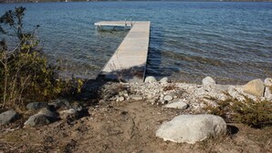 Eine hölzerne Anlegestelle erstreckt sich über einen ruhigen See mit felsigen Ufern und spärlicher Vegetation.