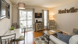 A living room with a sofa, a dining table with chairs, a TV, and a wall-mounted sign reading "Nashville". - Stunning River View Condo Near Downtown With Free Covered Parking (Nashville)