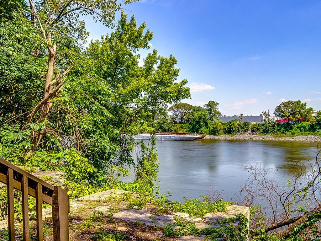 A serene lakeside view with a wooden deck, lush greenery, and a distant boat on the water.