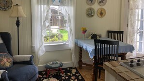 A cozy room with a blue armchair, a small stool, a dining table with a blue tablecloth, and a kitchen area with a stove. - Private Garden Cottage In Mendocino's Historic Preservation District (Mendocino)
