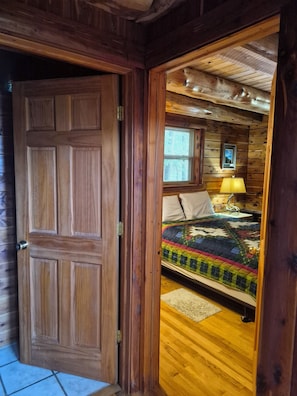 A wooden door leading to a room with a bed, a window, and a lamp. - Deer Cabin Of Deer Lodge Cabin Rentals is a Secluded Ozark Cedar Log Cabin (Jasper)
