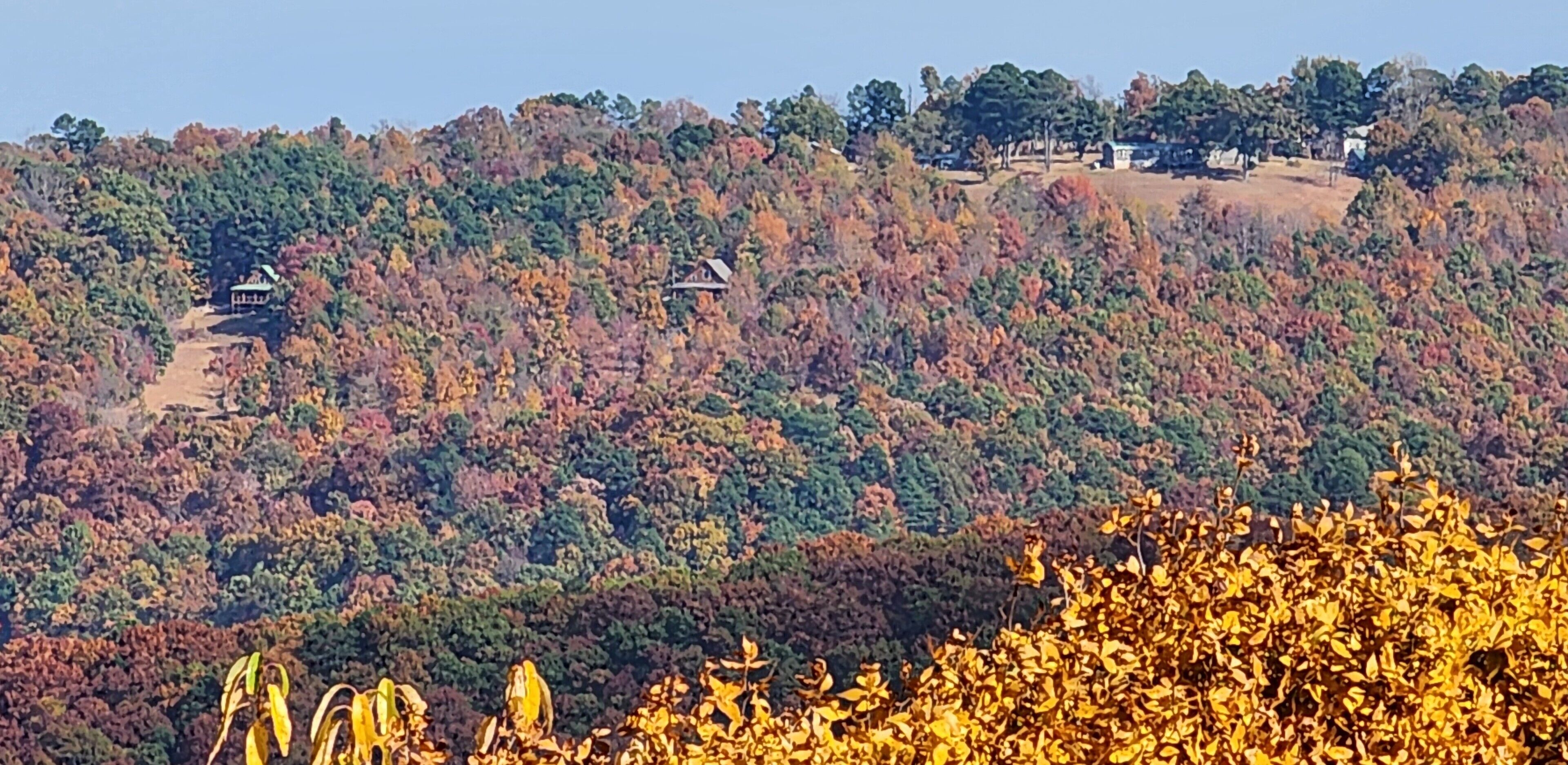 A hilly landscape with autumn foliage, a small house, and a clear sky.