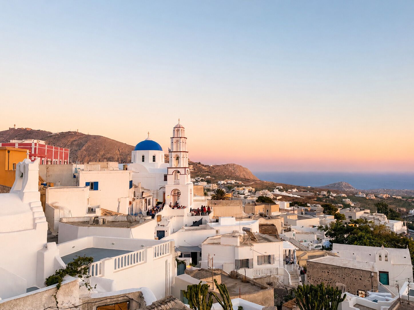 Uma cidade costeira com edifícios brancos, uma igreja imponente com cúpula azul e vista ampla para o mar.