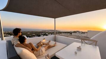 A couple relaxing on a balcony with a city view at sunset.