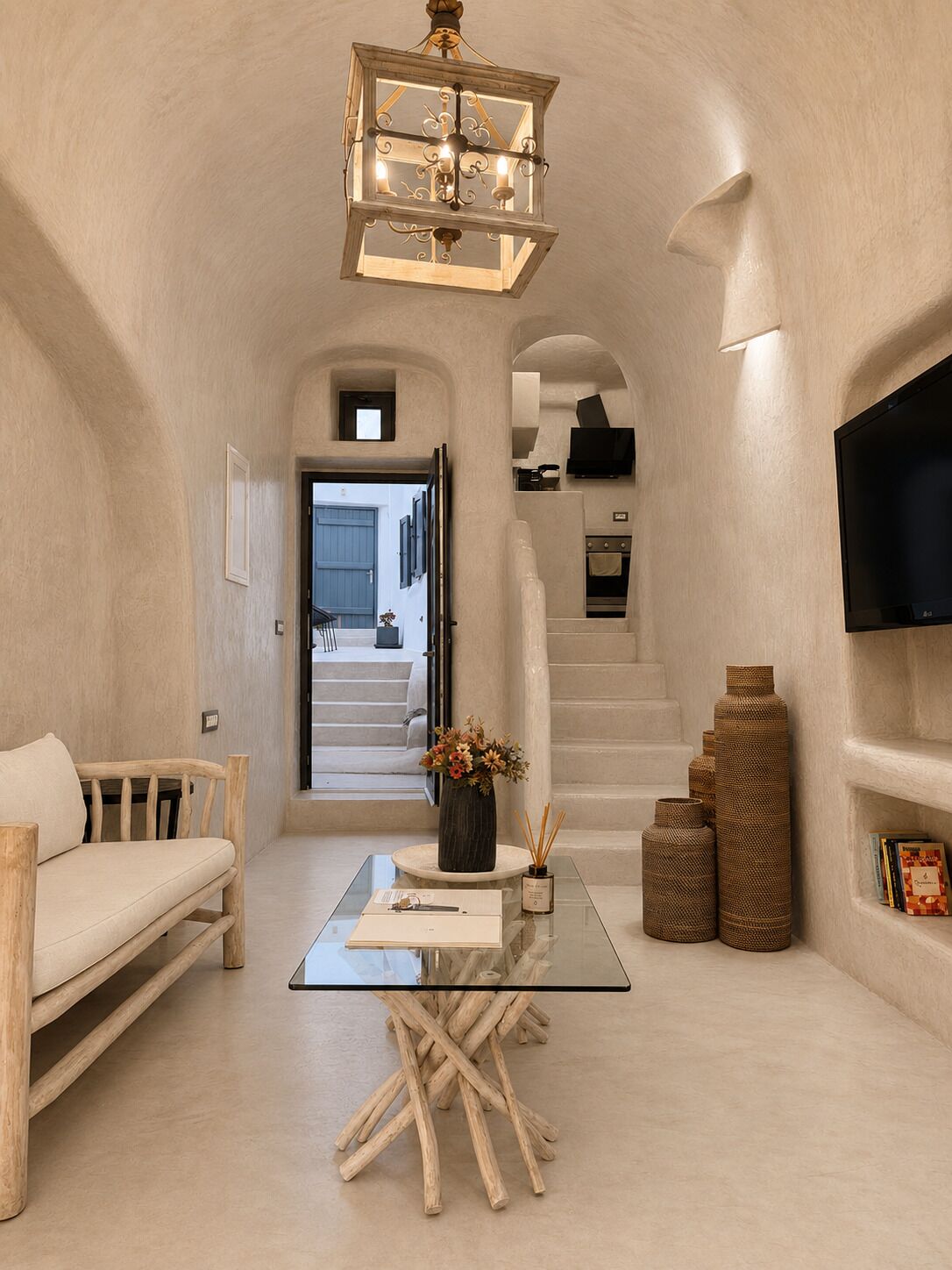 Un interior espacioso con una mesa de vidrio, muebles de madera, un candelabro y una escalera que lleva a un balcón.