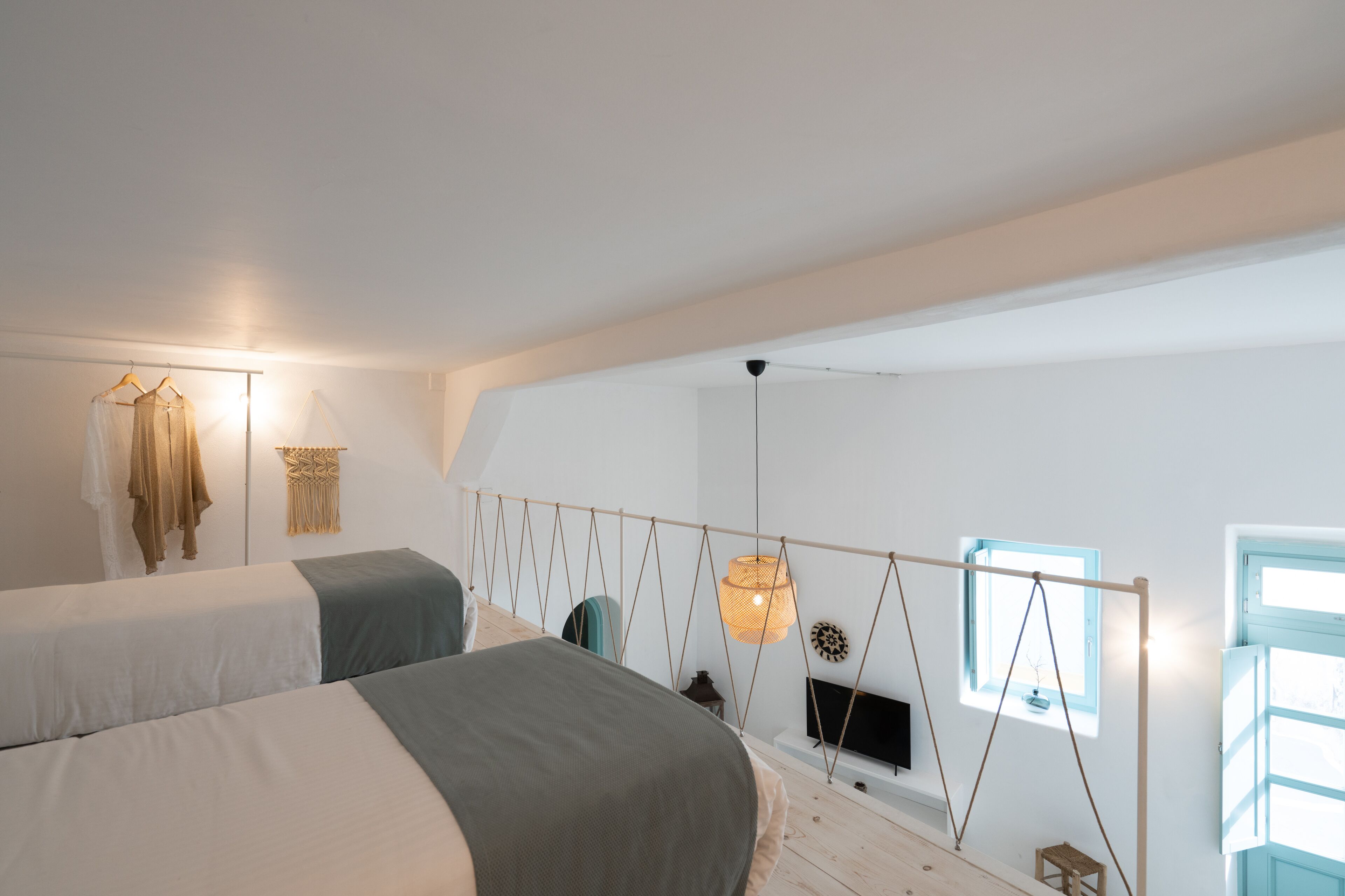 Ein Schlafzimmer mit zwei Betten, einer Hängeleuchte, einem Fenster und einem an der Wand montierten Fernseher.