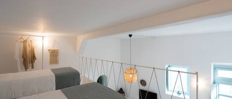 Ein Schlafzimmer mit zwei Betten, einer Hängeleuchte, einem Fenster und einem an der Wand montierten Fernseher.