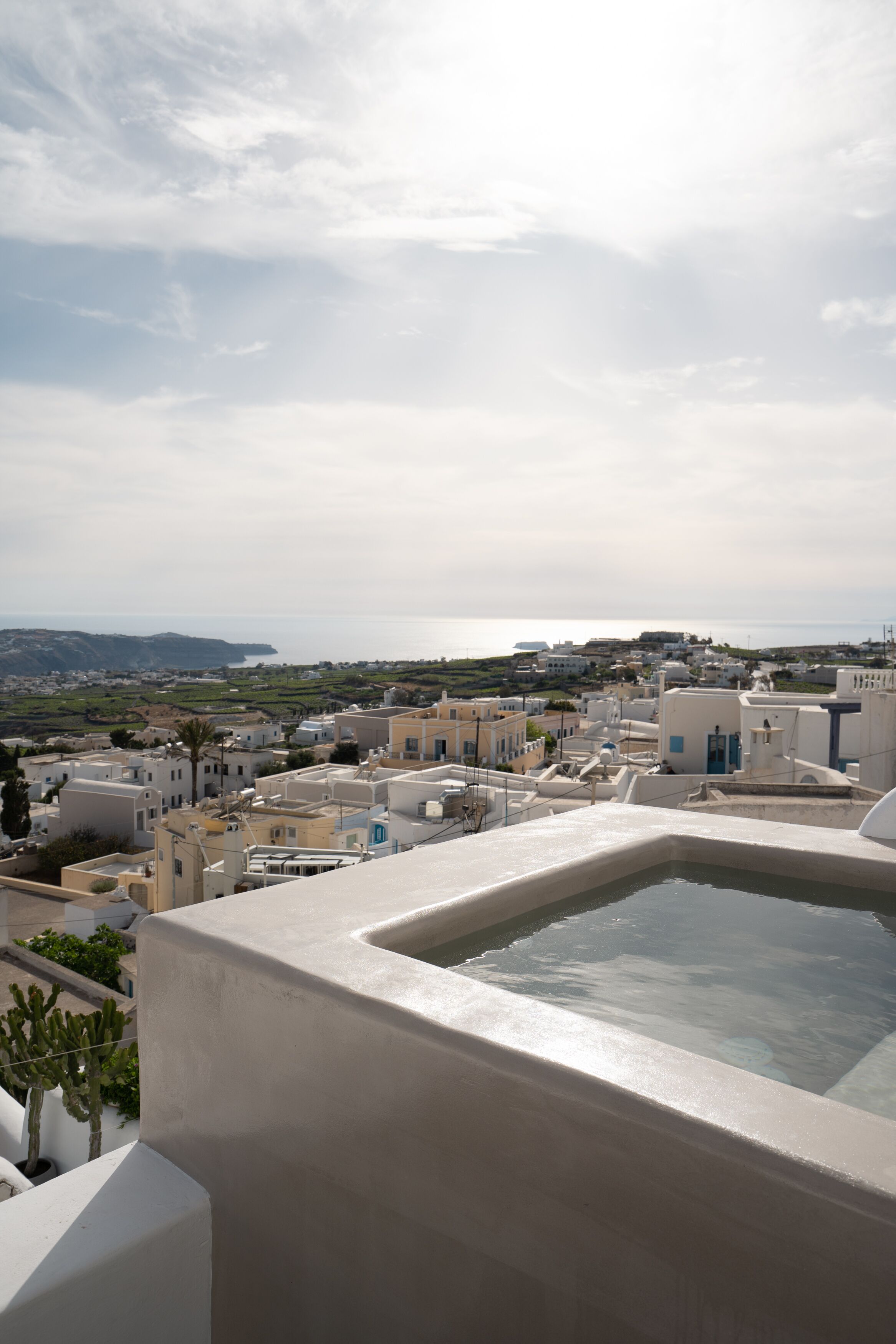 A rooftop terrace with a pool, overlooking a coastal town with traditional architecture and a clear view of the sea.