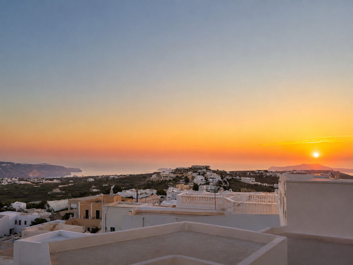 A coastal town at sunset with white buildings and a clear sky.