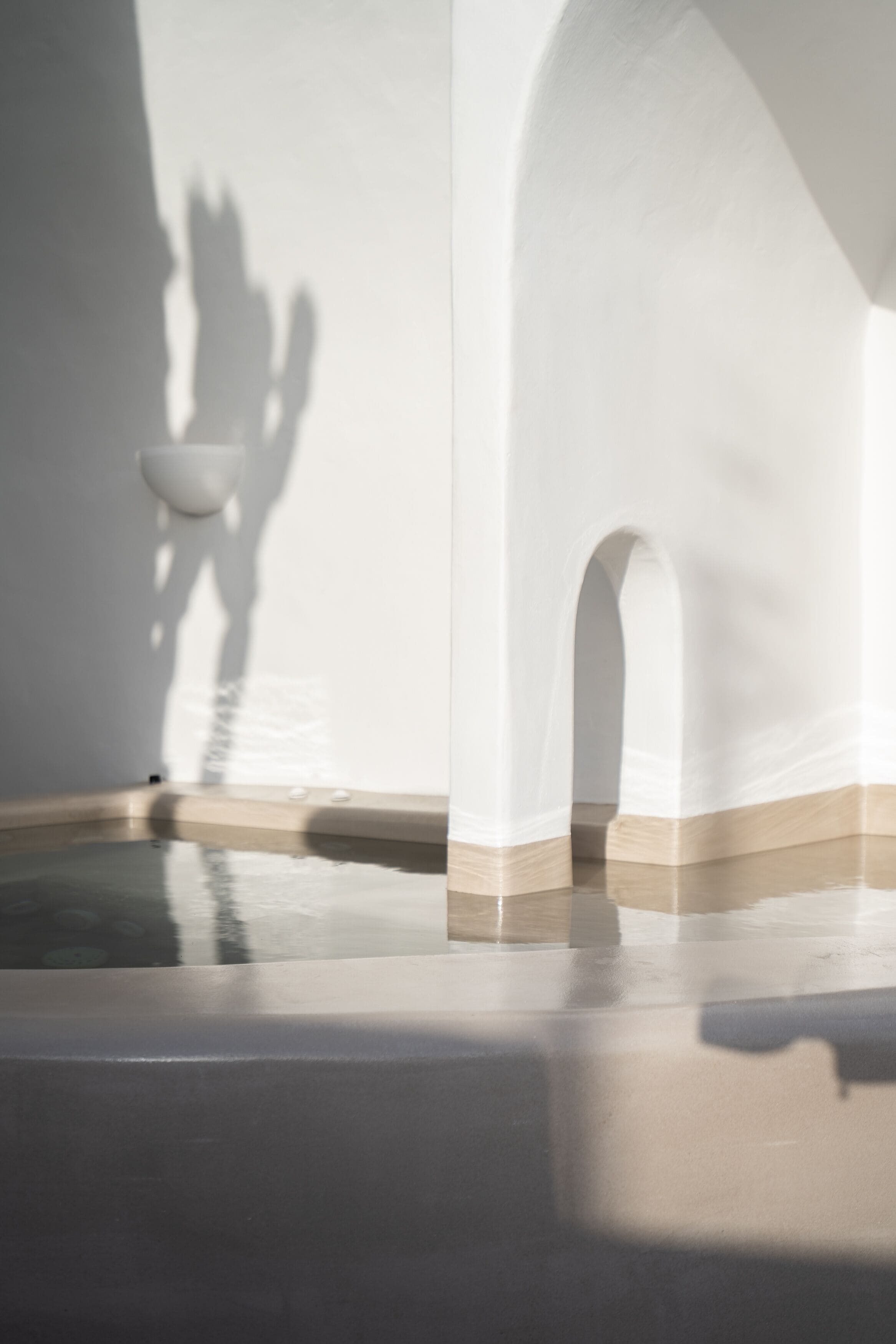 A modern interior with a minimalist design, featuring a pool area with a clear reflection on the floor, white walls, and a shadow cast by a person.