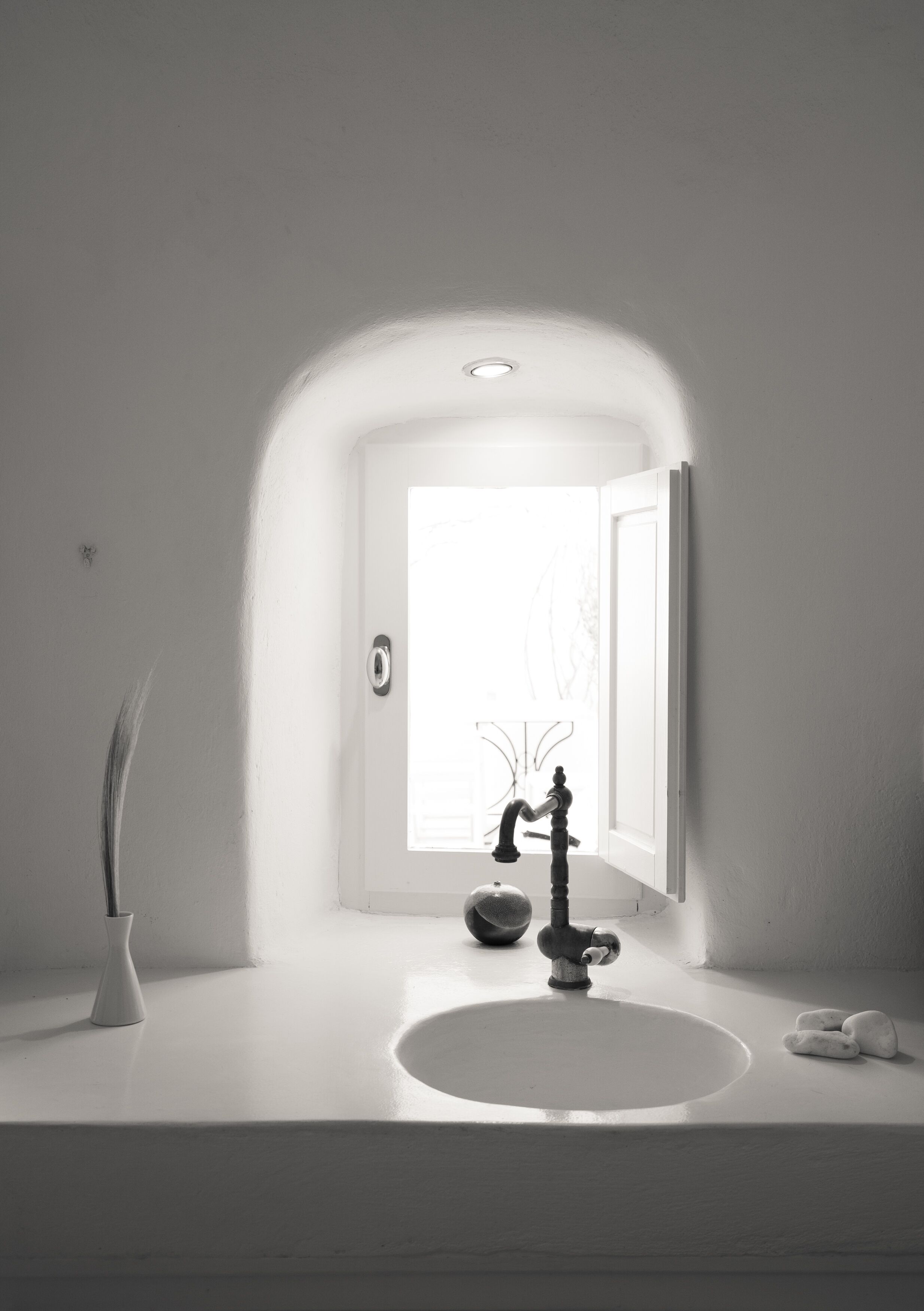 A minimalist bathroom with a white sink, a vintage-style faucet, and a vase with a plant.