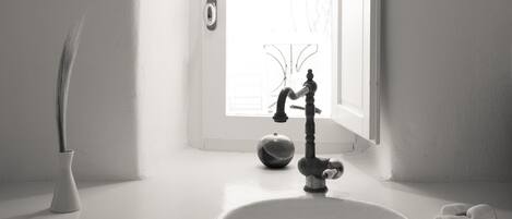 A minimalist bathroom with a white sink, a vintage-style faucet, and a vase with a plant.