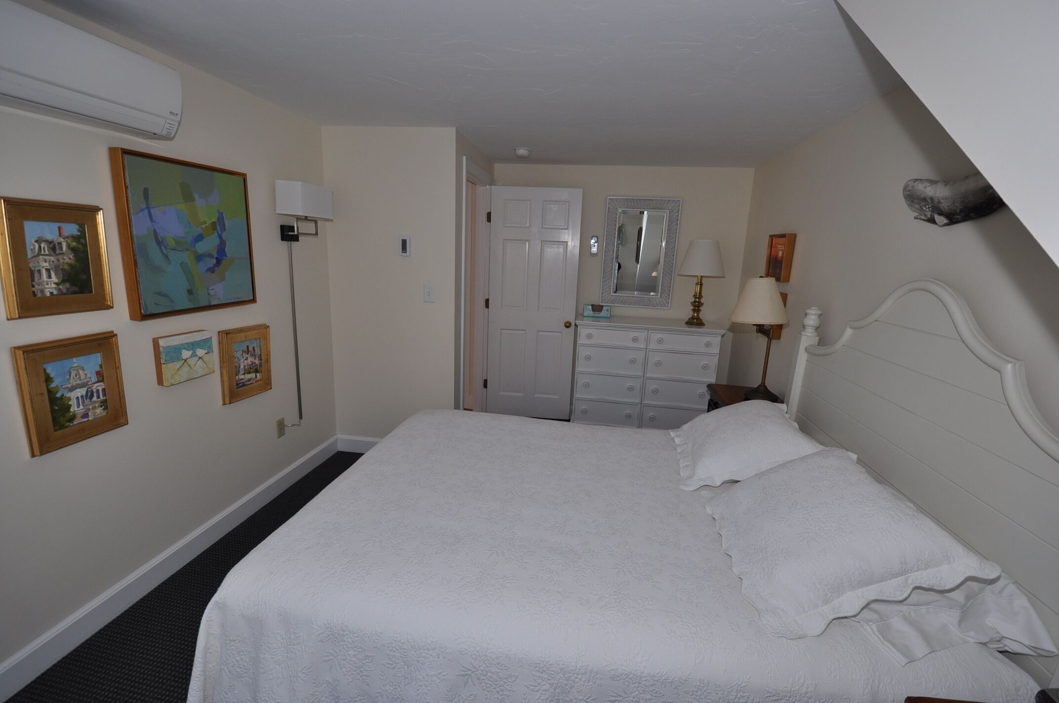 Een slaapkamer met een groot bed, een kaptafel, een spiegel en verschillende ingelijste foto’s aan de muur.