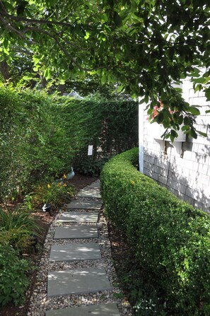 Un sendero de piedra bordeado de vegetación exuberante y un edificio blanco con una ventana.