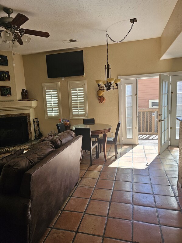 A living room with a brown leather sofa, a dining table with chairs, a ceiling fan, and a fireplace.