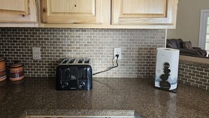 Una cucina con mobili in legno, un tostapane nero e uno schienale in mattoni.