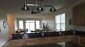 Una cocina con encimera de granito, armarios de madera, ventilador de techo y ventana con persianas.