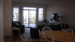 Una sala de estar con una mesa de comedor de madera, sillas blancas, un sofá y un televisor.