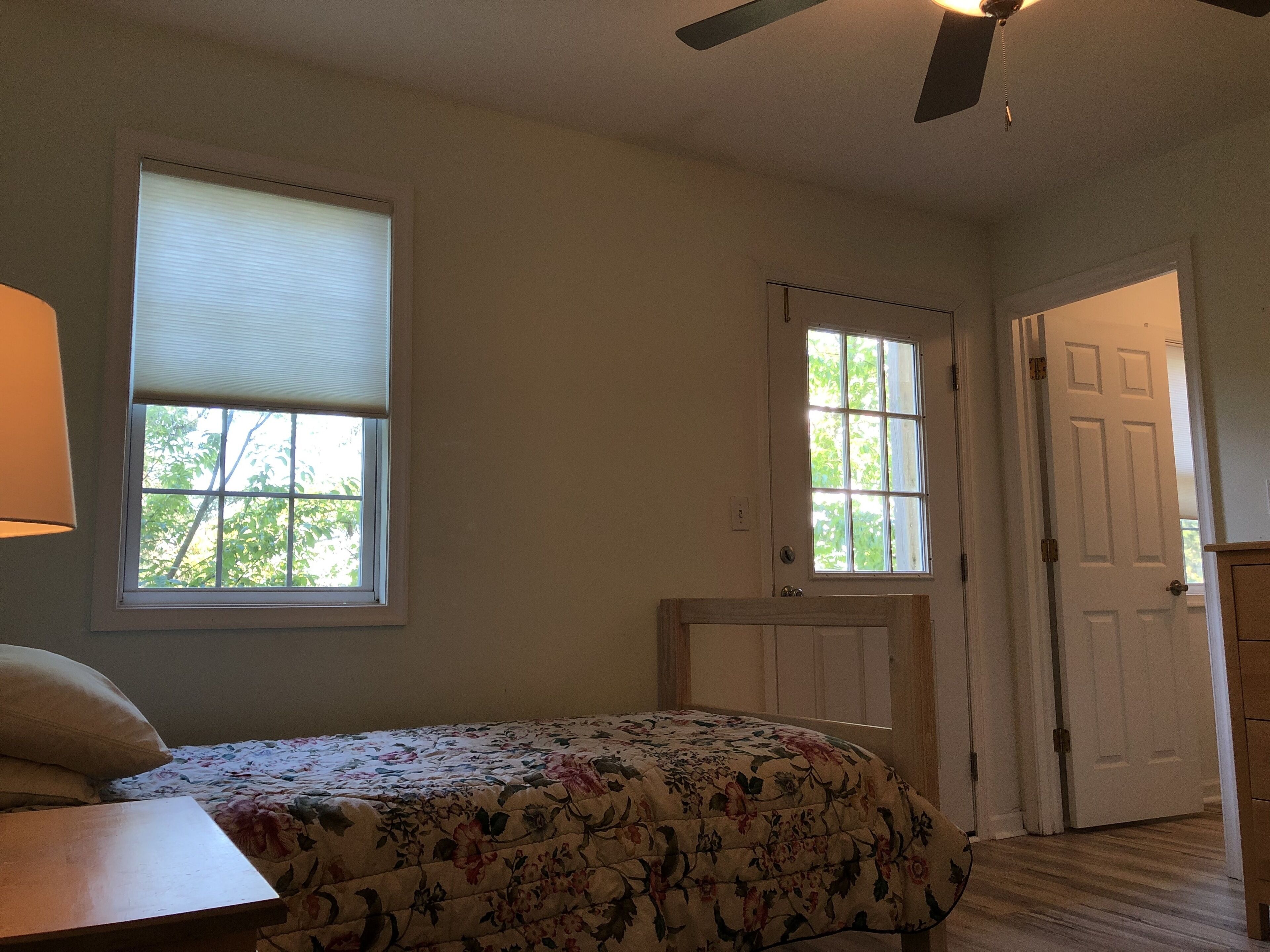 Une chambre à coucher avec un lit, deux fenêtres, un ventilateur de plafond et une porte.