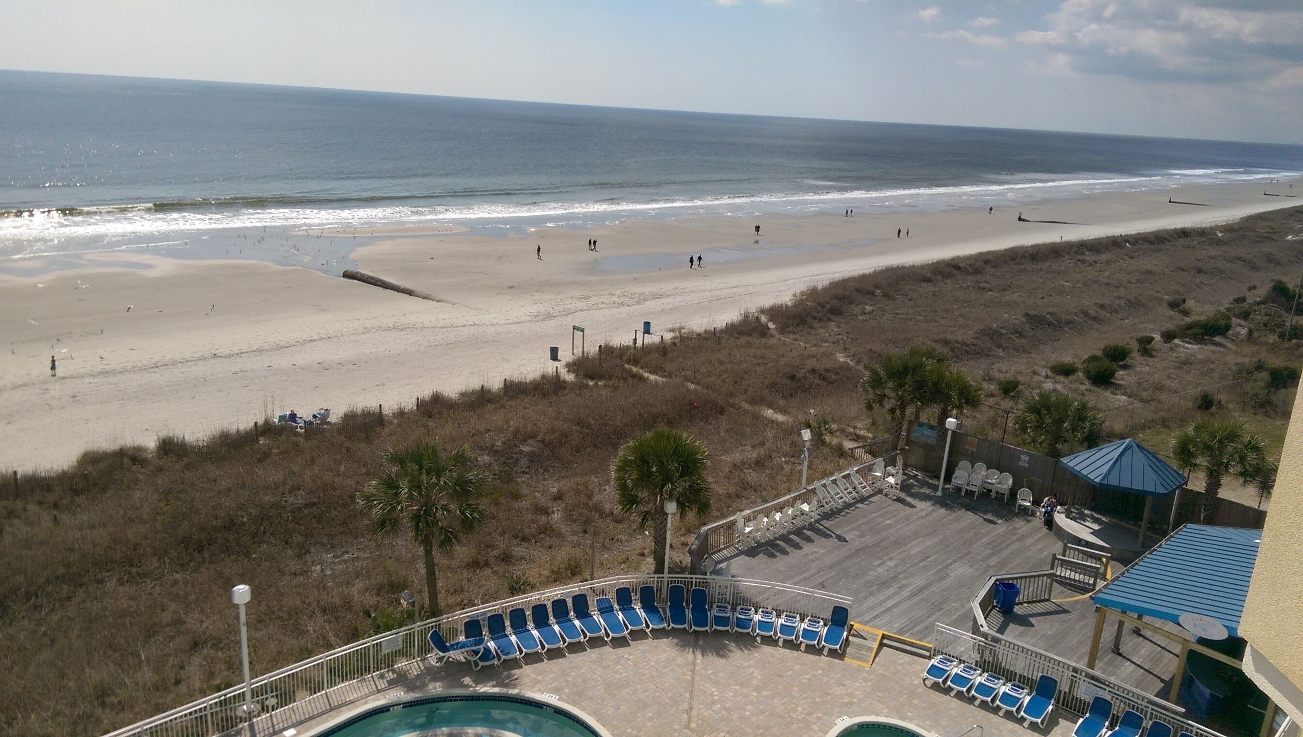 Blick auf einen Strand mit Poolbereich, Liegestühlen und einer überdachten Sitzgelegenheit.