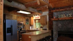 Une cuisine rustique avec des meubles en bois, une cheminée en pierre et un coin bar avec des tabourets.