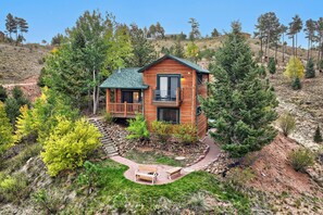 A cabin with a balcony, surrounded by trees and a stone pathway leading to a bench. - Pikes Peak Ranch - Elk Ridge Cabin (Woodland Park)