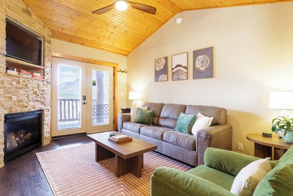 A cozy living room with a stone fireplace, a wooden ceiling, and a green couch. - Pikes Peak Ranch - Elk Ridge Cabin (Woodland Park)