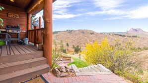 A wooden porch with a grill and outdoor seating, overlooking a hilly landscape with a mountain in the distance. - Pikes Peak Ranch - Elk Ridge Cabin (Woodland Park)