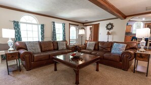 Un salon spacieux avec un grand canapé d’angle en cuir marron, une table basse en bois et une grande fenêtre agrémentée de rideaux.