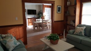 Ein Wohnzimmer mit einem grünen Sofa, einem weißen Couchtisch mit einer Pflanze und einem Essbereich mit Holztischen und Stühlen.