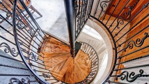 A spiral staircase with a wooden handrail and black metal balusters. - Chateau Royal East (Yosemite National Park)