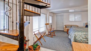 A bedroom with a wooden staircase, a rocking chair, a bed with a blue quilt, and a small table with a pinecone decoration. - Chateau Royal East (Yosemite National Park)