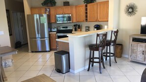 A modern kitchen with wooden cabinets, stainless steel appliances, a central island with bar stools, and a small trash can. - Golf Lovers' Haven in PGA Village  (Port St Lucie)