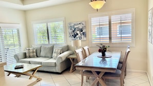 A dining area with a glass table, wooden chairs, a sofa with patterned cushions, and a ceiling light fixture. - Golf Lovers' Haven in PGA Village  (Port St Lucie)