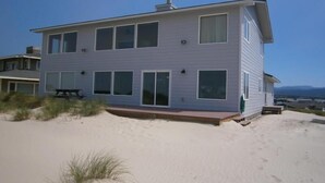 Een tweelaags strandhuis met een plat dak, grote ramen en een terras.
