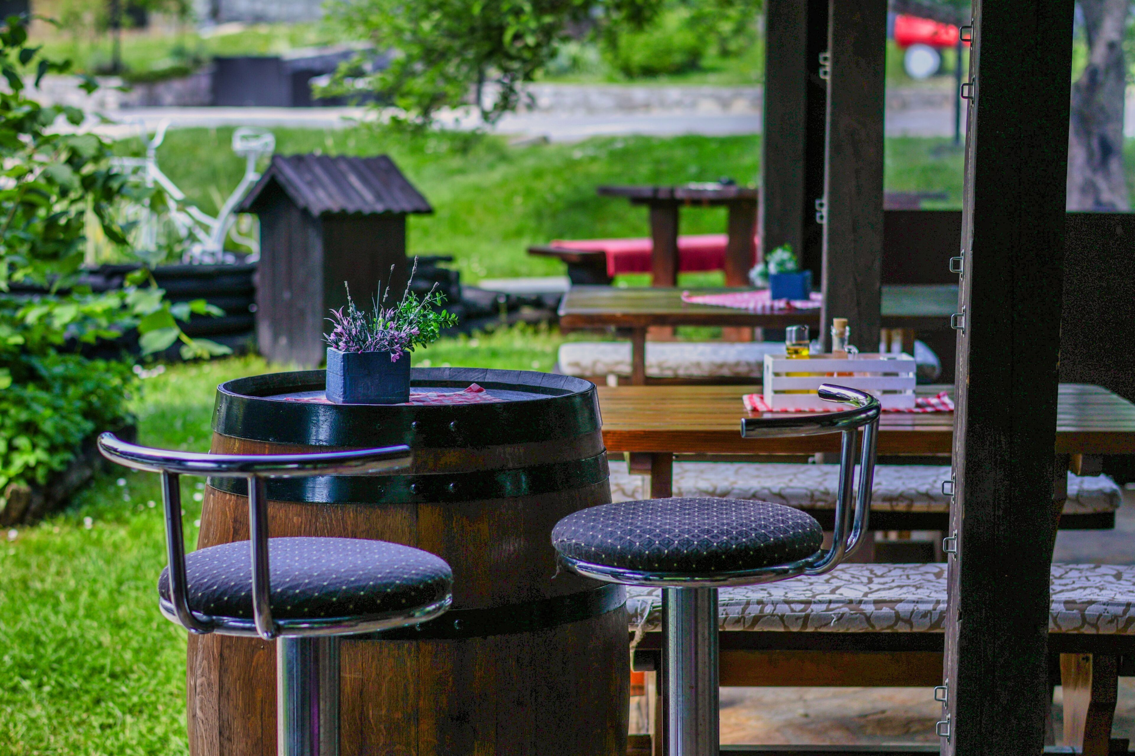 Espace extérieur aménagé avec des tonneaux en bois et des chaises en métal, une table en bois et un petit jardin.