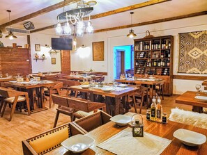 Un restaurante con varias mesas y sillas de madera, una estantería para vinos y un televisor en la pared.