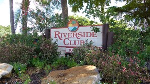 Letrero del Riverside Club rodeado de exuberante vegetación y rocas.