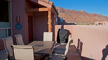 An outdoor patio with a table and chairs, a wooden pergola, and a mountain view.