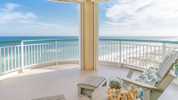 Un balcon avec vue sur l’océan et la plage, comprenant une table agrémentée d’objets décoratifs, une chaise et un petit banc.