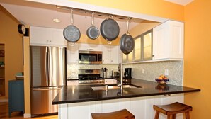 A modern kitchen with stainless steel appliances, a black countertop, and hanging pots. - 300 paces-1/2 Block to McKinley Beach, Fire Pit, Screened Gazebo,
Outdoor Shower (Union Pier)