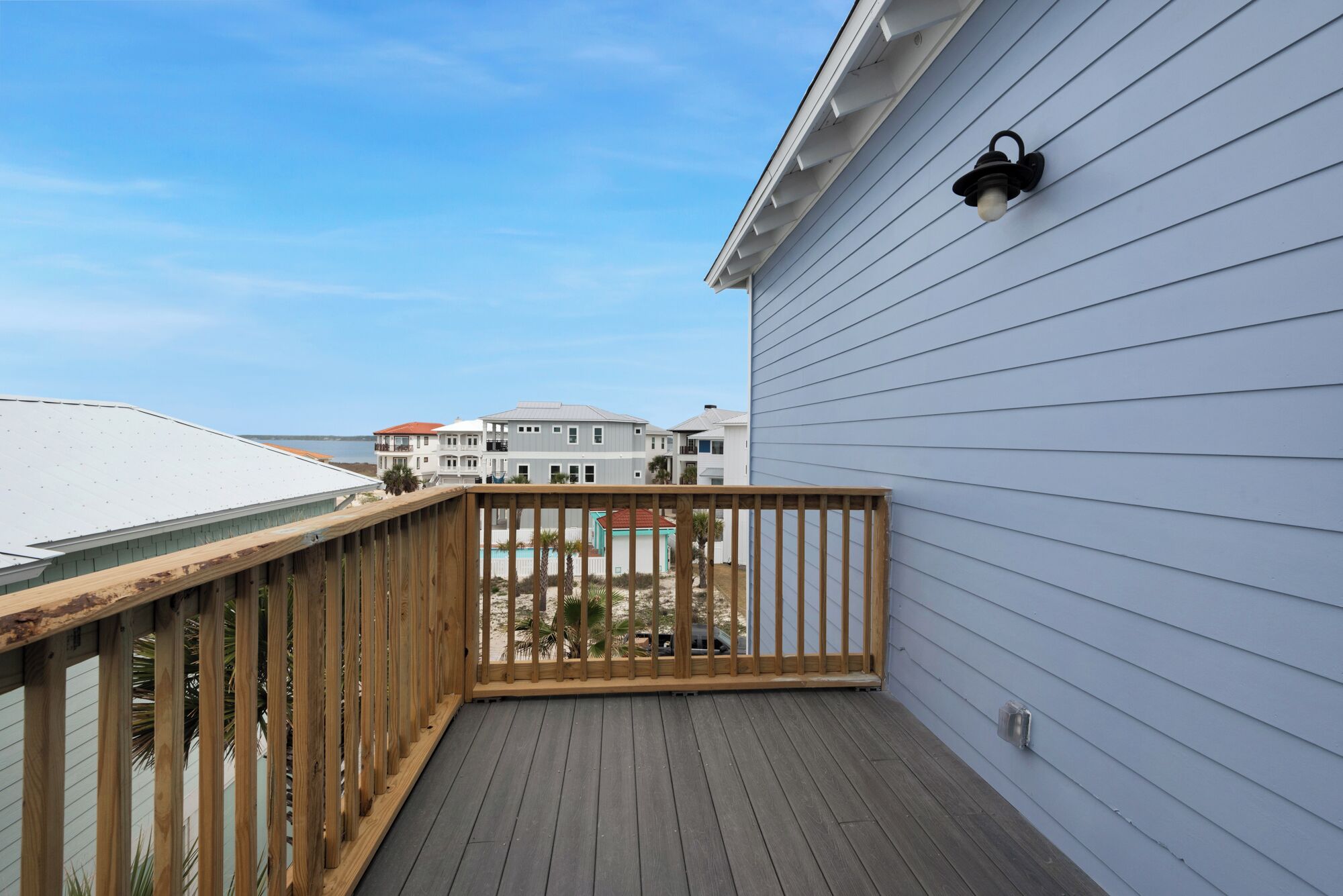 Une terrasse en bois avec une rambarde, un luminaire fixé au mur et une vue sur une propriété située en bord de mer.