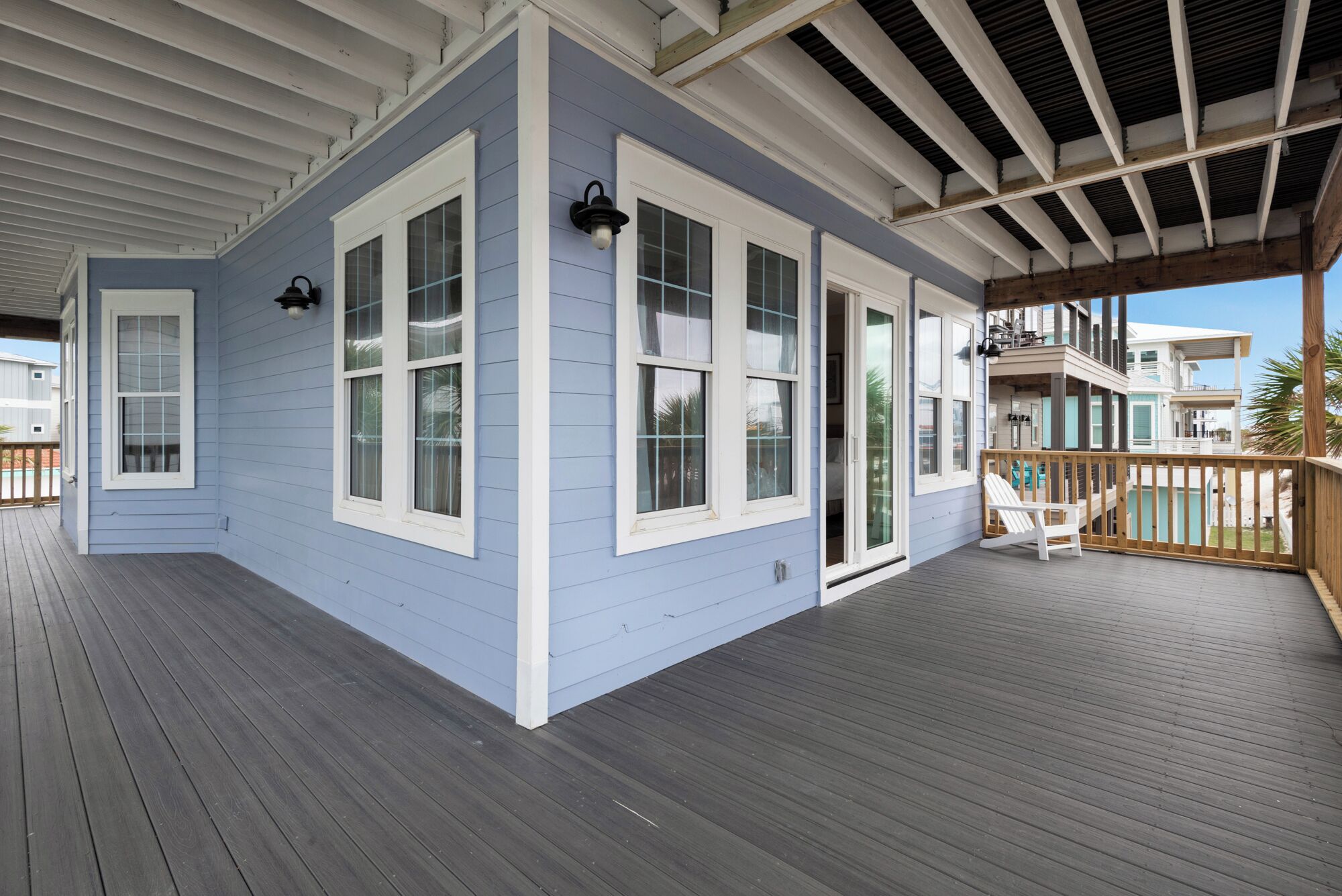 A covered porch with a wooden deck, white-framed windows, and a view of neighboring houses.