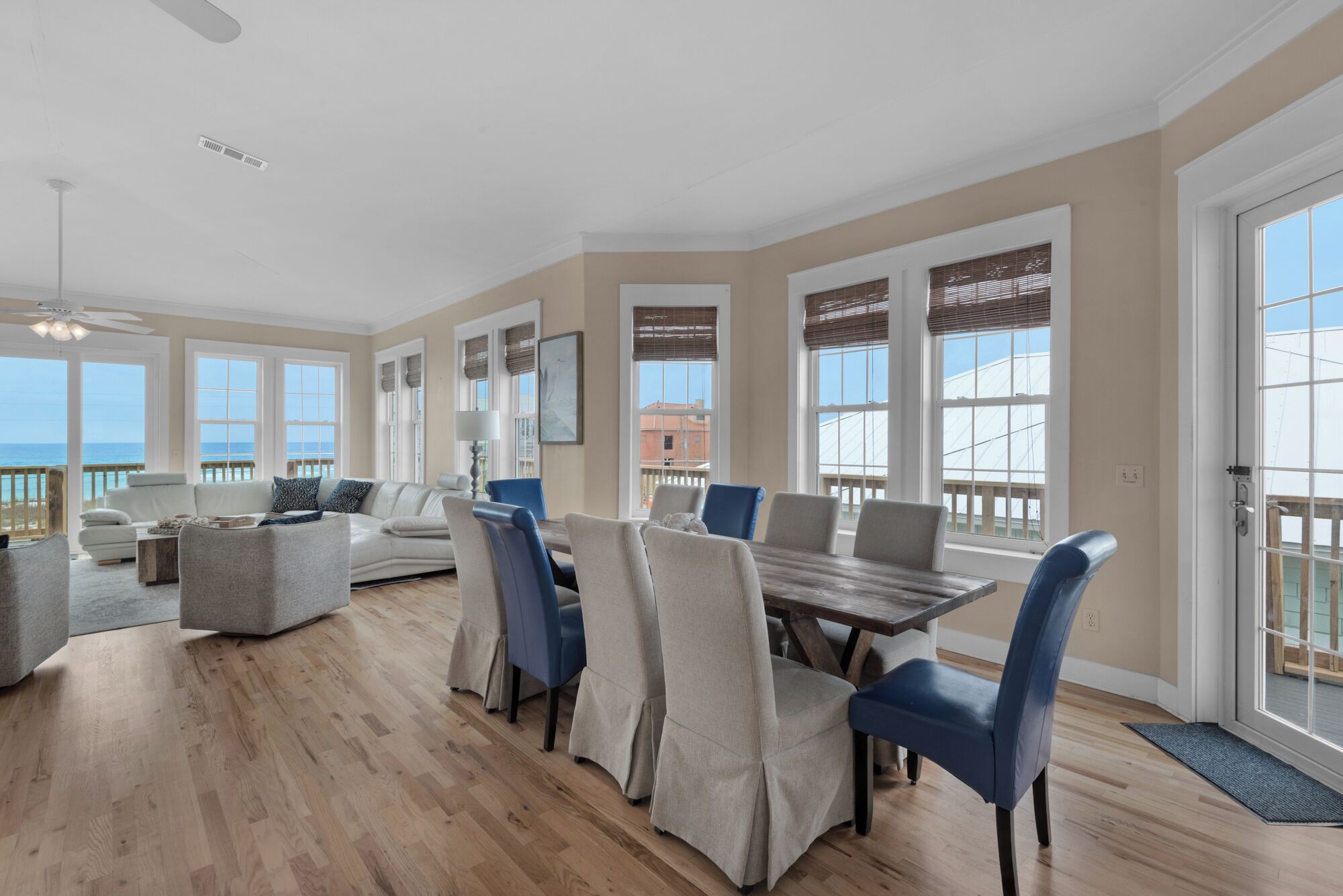 A spacious living room with a large dining table, comfortable seating, and large windows offering a view of the ocean.