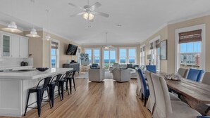 A spacious living area with a large wooden dining table, multiple seating options, and a view of the ocean through large windows.