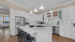 A modern kitchen with white cabinetry, a central island with bar stools, stainless steel appliances, and pendant lighting.