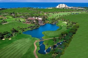 Un campo de golf con un estanque, un club de campo y vistas al océano.